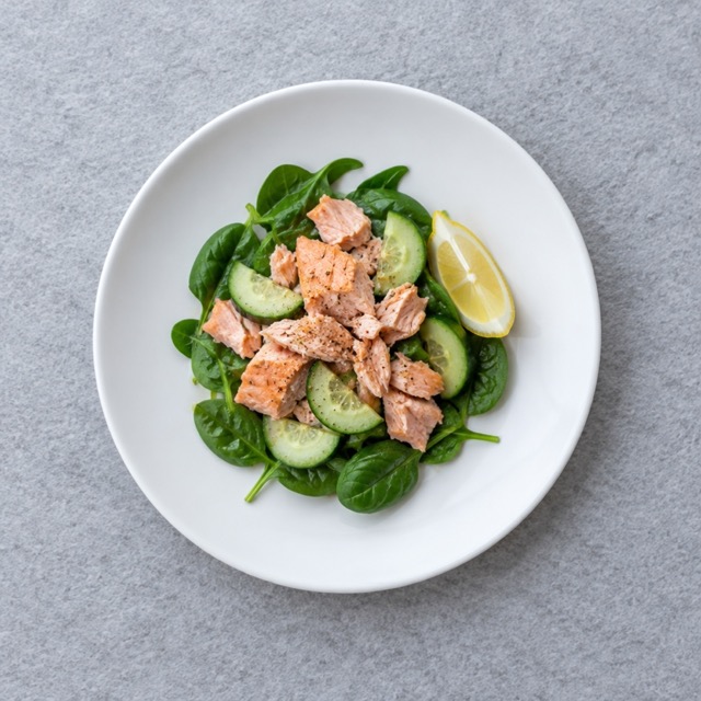 Salmon fillet on a bed of spinach salad plated on a white dish, a realistic home lunch portion for one